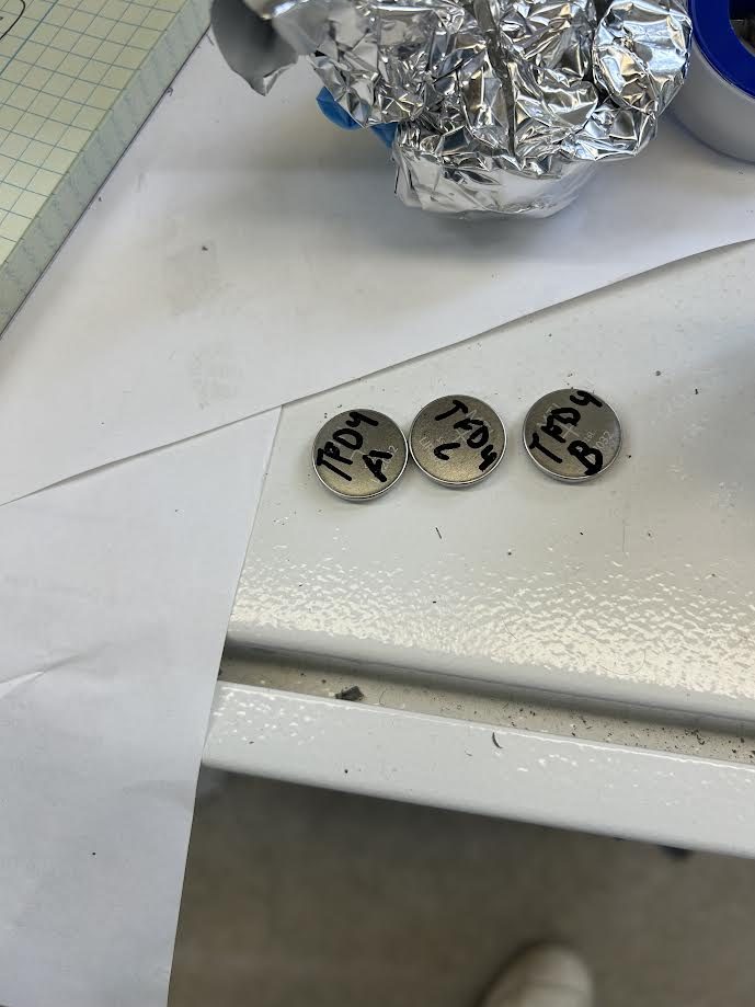 Three labeled coin cells on a white bench